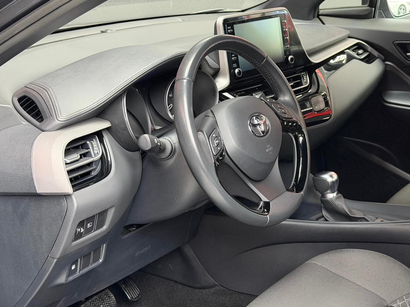 Interior Toyota C-HR gris con salpicadero, pantalla táctil y mandos de clima bizona